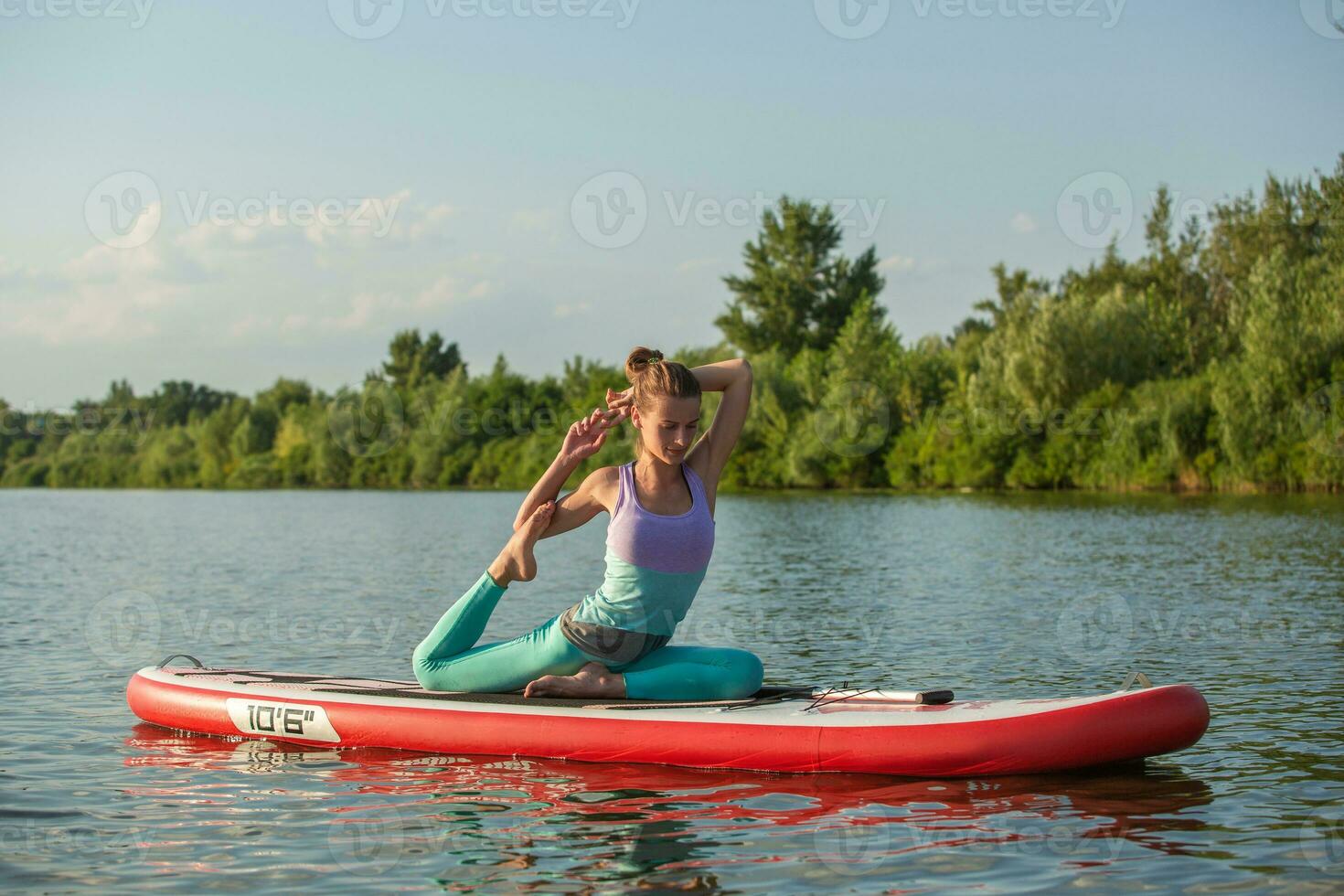 Young woman doing yoga on sup board with paddle. Meditative pose, side view - concept of harmony with the nature photo
