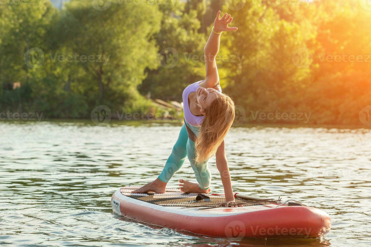 Young woman doing yoga on sup board with paddle. Yoga pose, side view - concept of harmony with the nature. photo