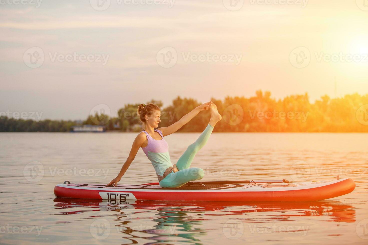 Young woman sitting on paddle board, practicing yoga pose. Doing yoga exercise on sup board, active summer rest photo