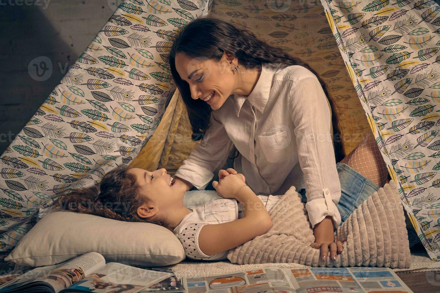 Mother and her daughter are in a teepee tent with some pillows. Happy family. photo