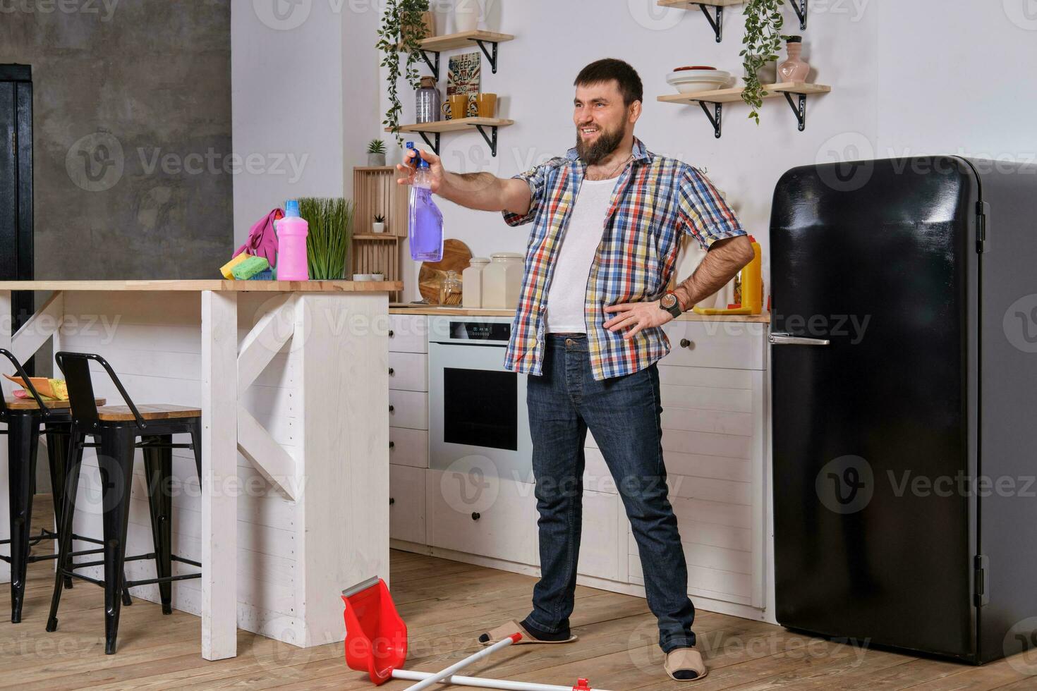 a man with a beard in the kitchen decided to take a break and fooling around with a sprinkler in his hands photo