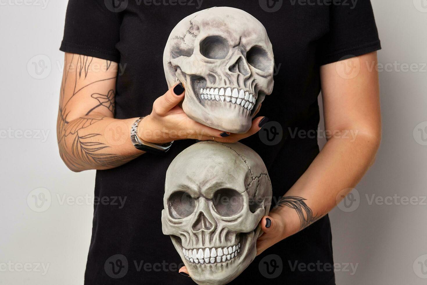 Tattooed hands of a woman in a black watch and clothes are holding a realistic model of a human skulls with teeth isolated on white. Close-up shot. photo