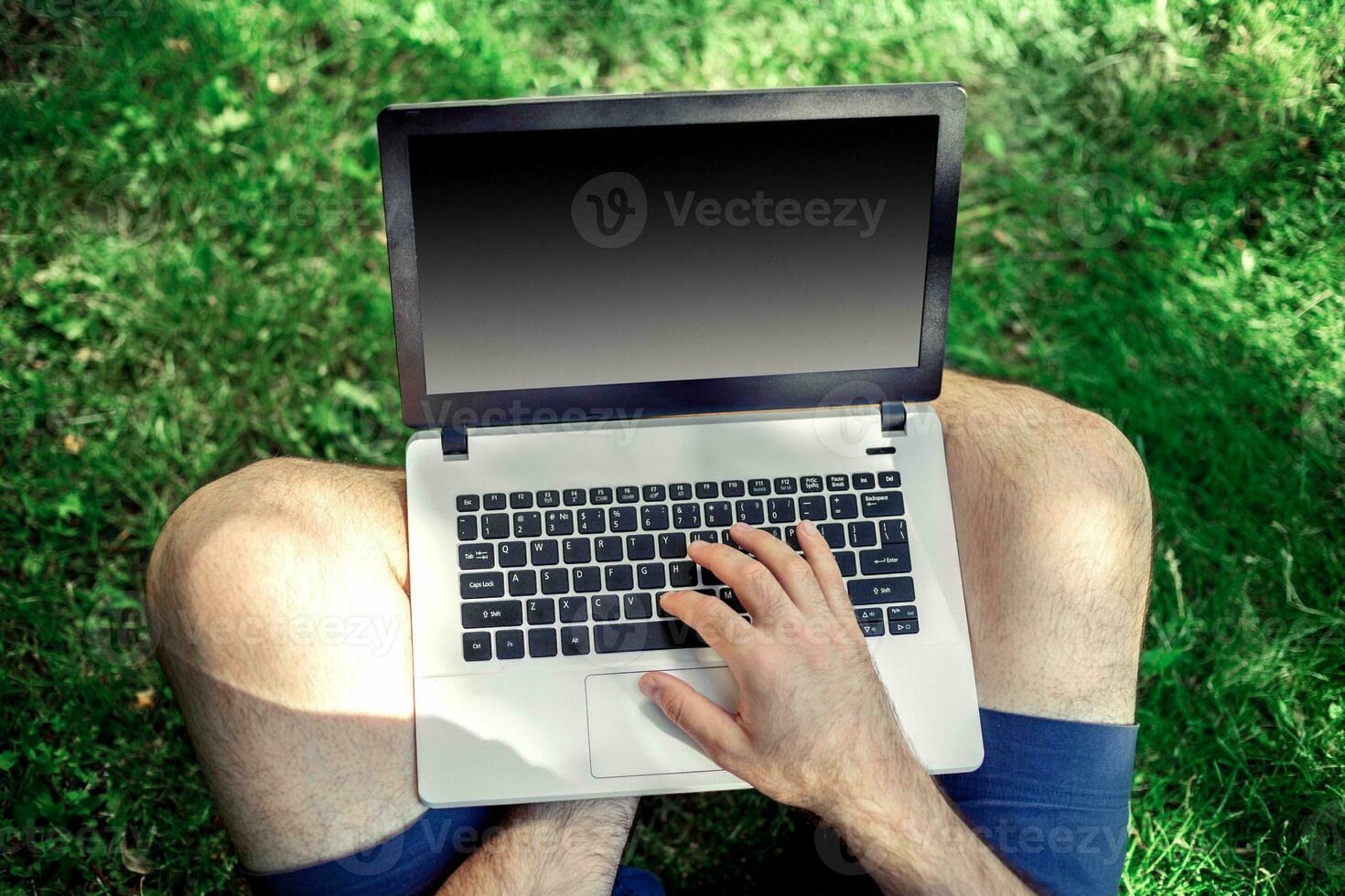 Young blogger sitting on grass and working with laptop photo