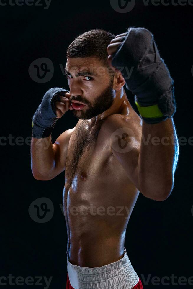 Boxing man ready to fight. Boxer with strong hands and clenched fists in blue straps against a black background photo