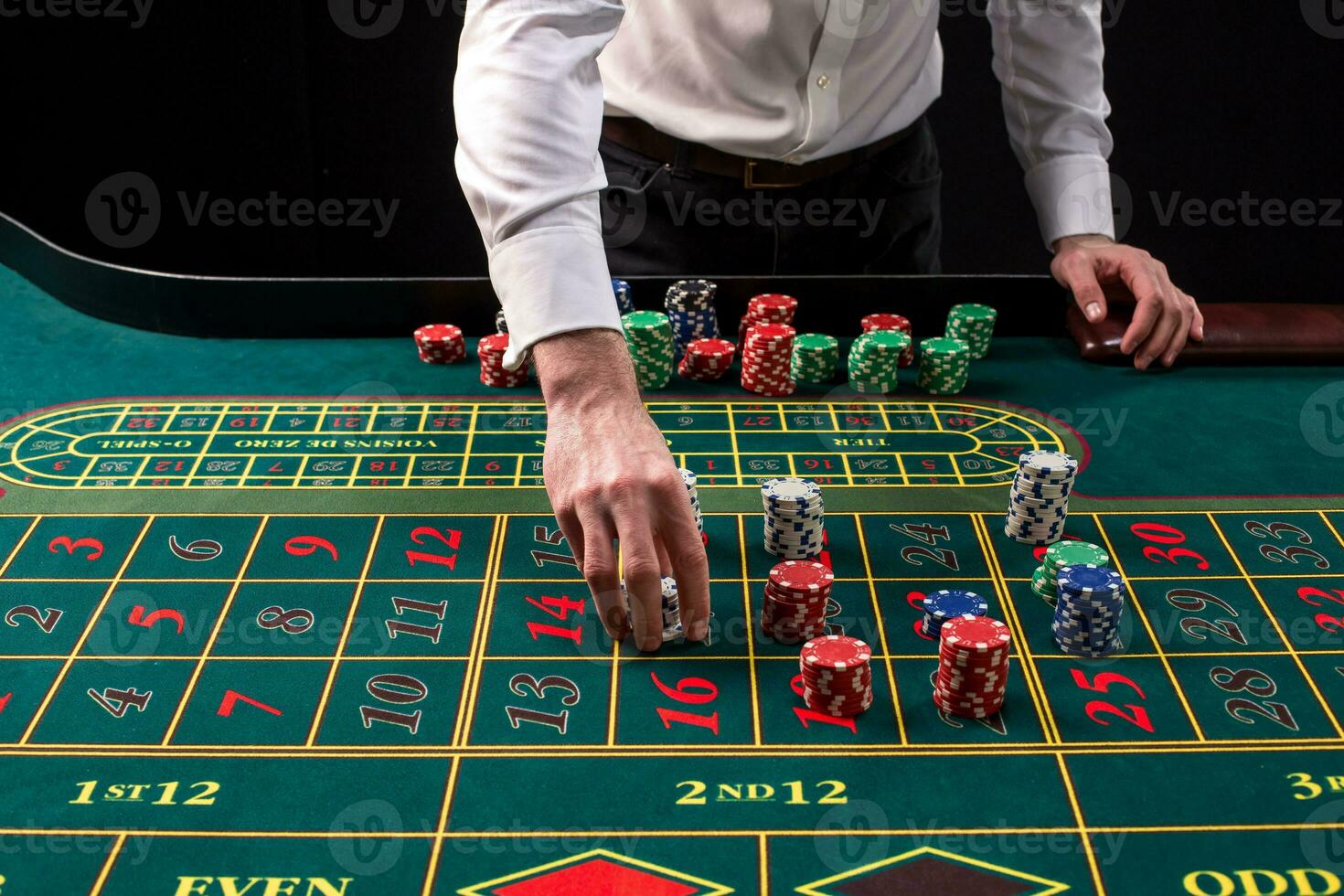 A close-up vibrant image of green casino table with roulette, with the hands of croupier and multicolored chips. photo