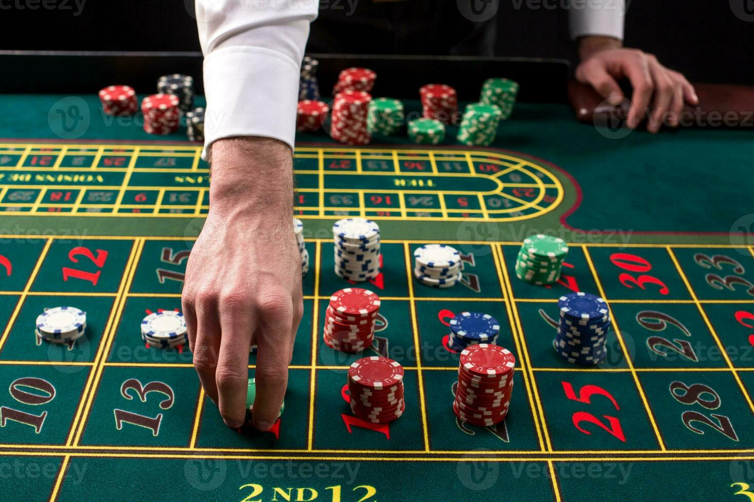 A close-up vibrant image of green casino table with roulette, with the hands of croupier and multicolored chips. photo