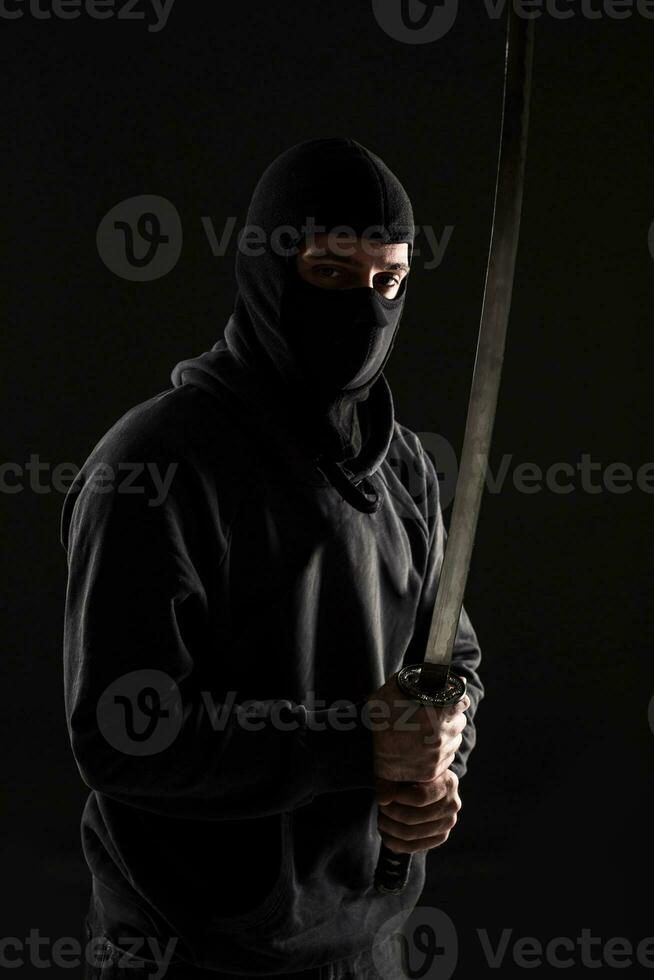 Man with balaclava and katana sword on black background photo