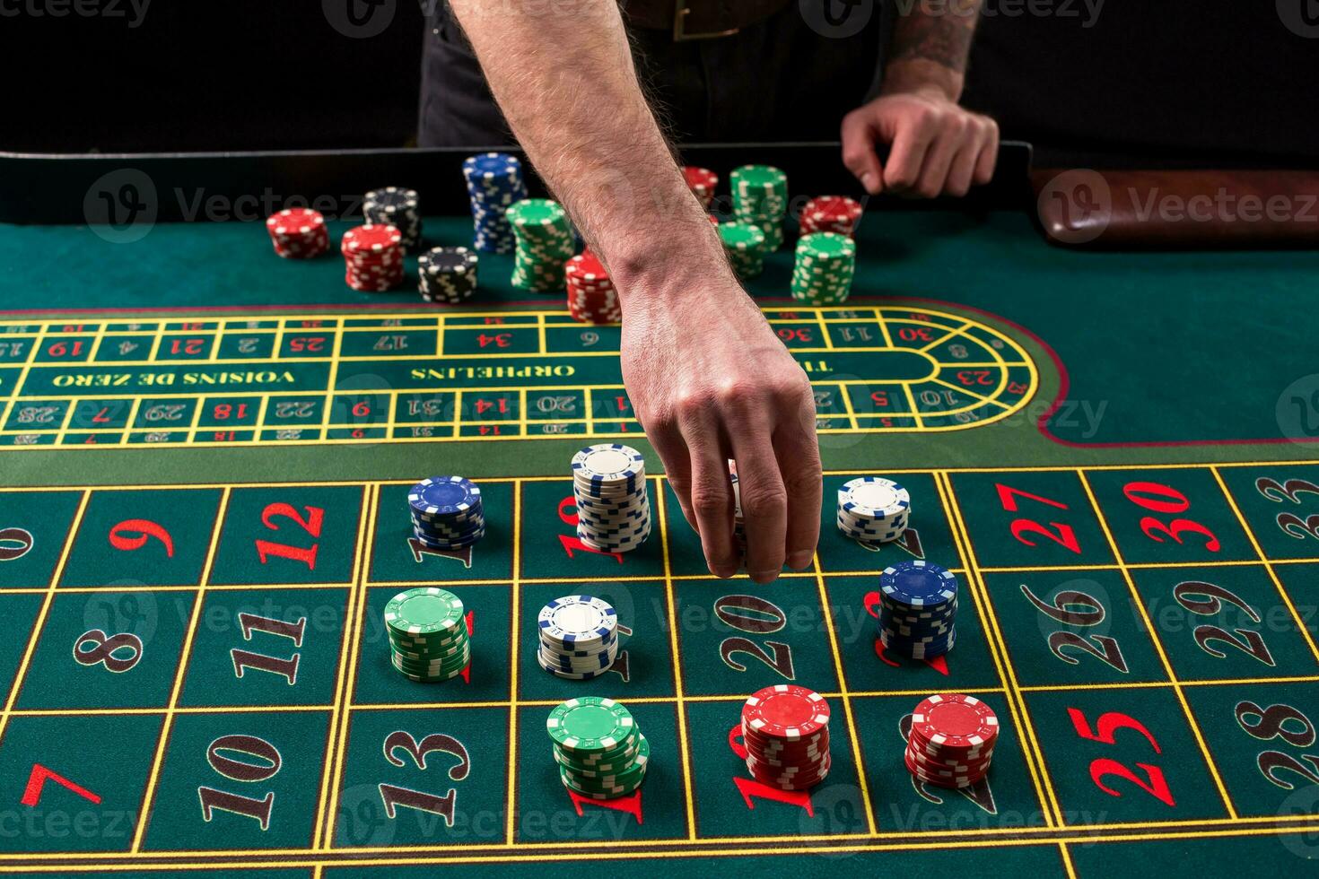 A close-up vibrant image of green casino table with roulette, with the hands of croupier and multicolored chips. photo