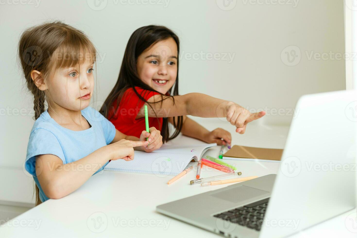 Two girls, the oldest and the youngest, are engaged at a table on a laptop. photo