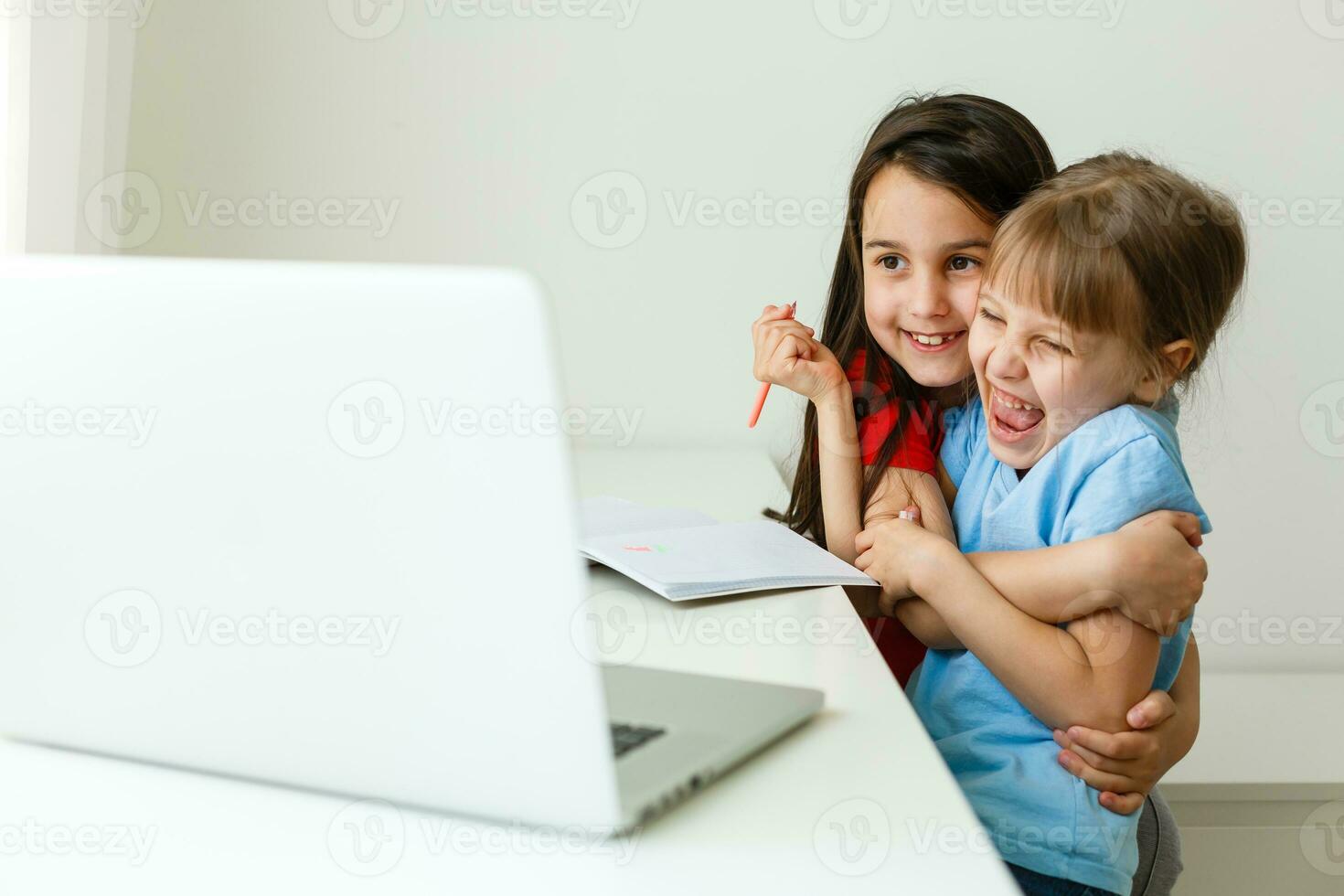 Two girls, the oldest and the youngest, are engaged at a table on a laptop. photo