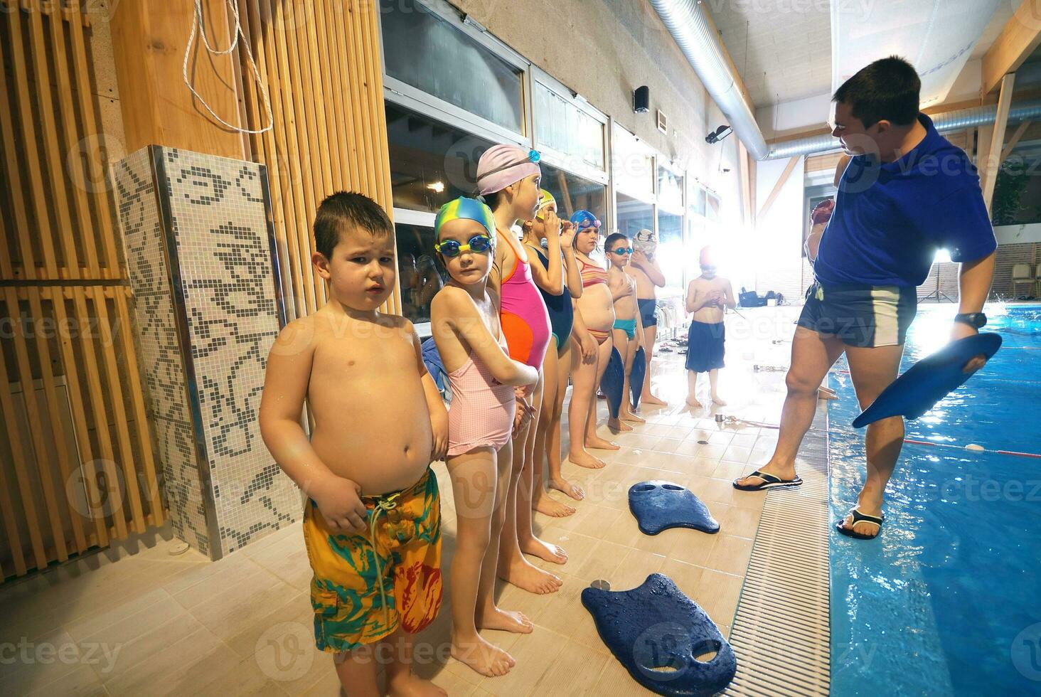a group of children in swimsuits standing in a pool photo