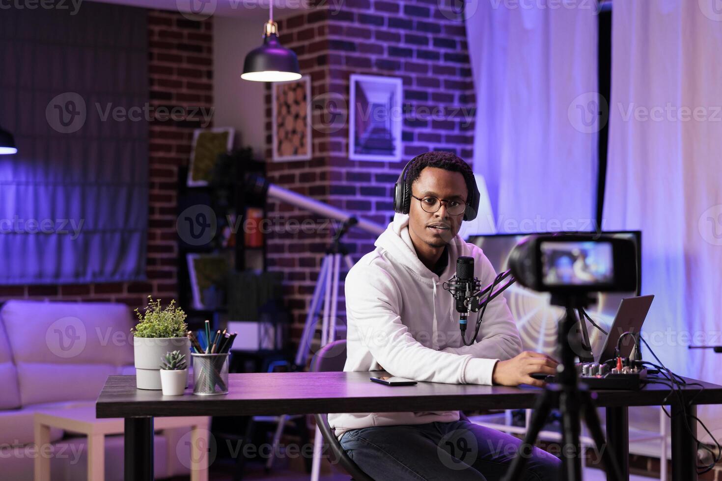 Vlogger recording internet show using modern camera, talking about international news and events subjects. Man filming live broadcast using professional gadgets in rgb lights studio photo