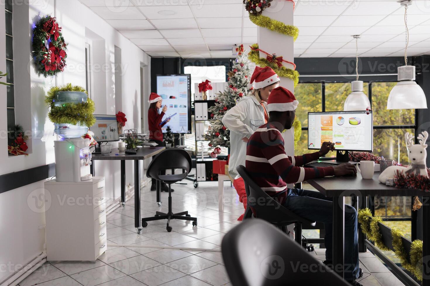 Focused multiethnic business people comparing marketing graphs at desk in Christmas ornate workplace. Corporate workers analysing data chart in festive decorated office during winter holiday photo