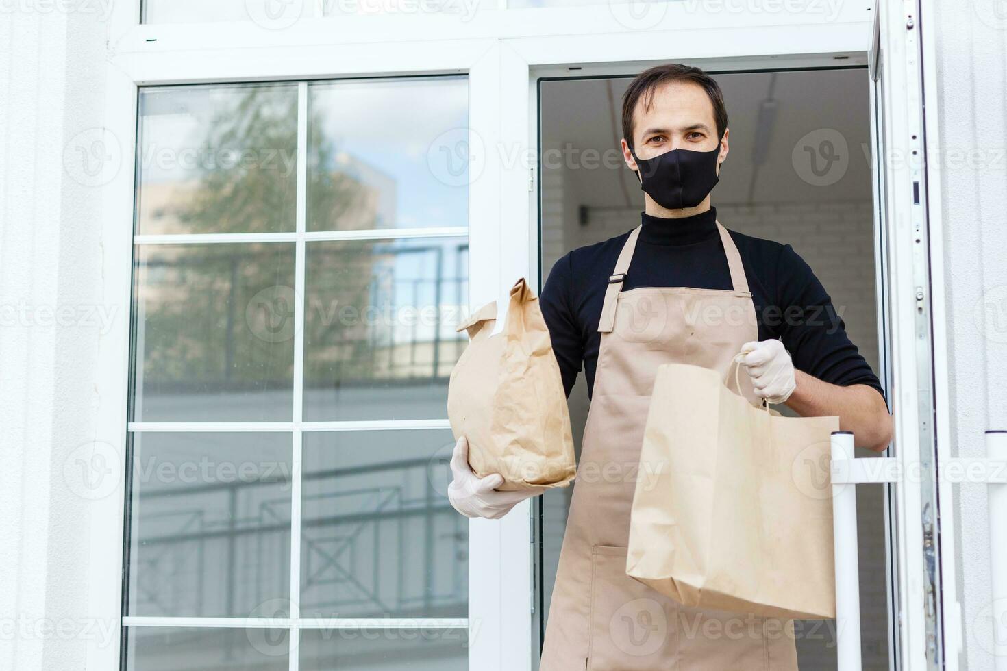 Delivery man holding paper bag with food, food delivery man in protective mask photo