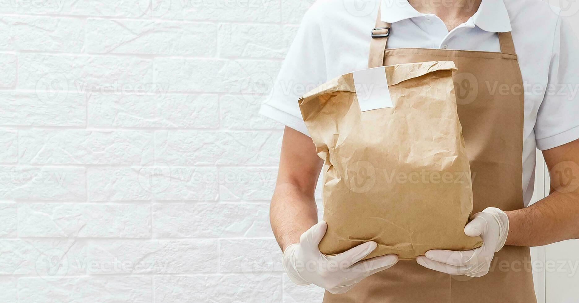 Holding take-out food paper bag, coffee cup. Light grey background, place to insert your text. Delivery man. photo