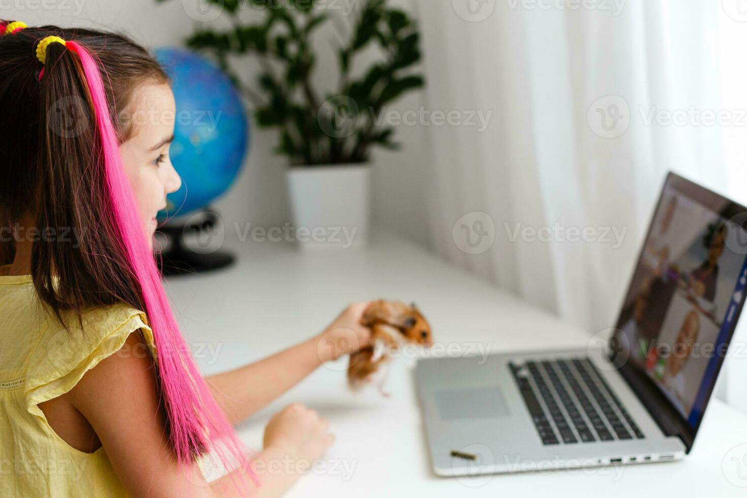 Cheerful young little girl with a pet hamster using laptop computer studying through online e-learning system at home. Distance or remote learning photo