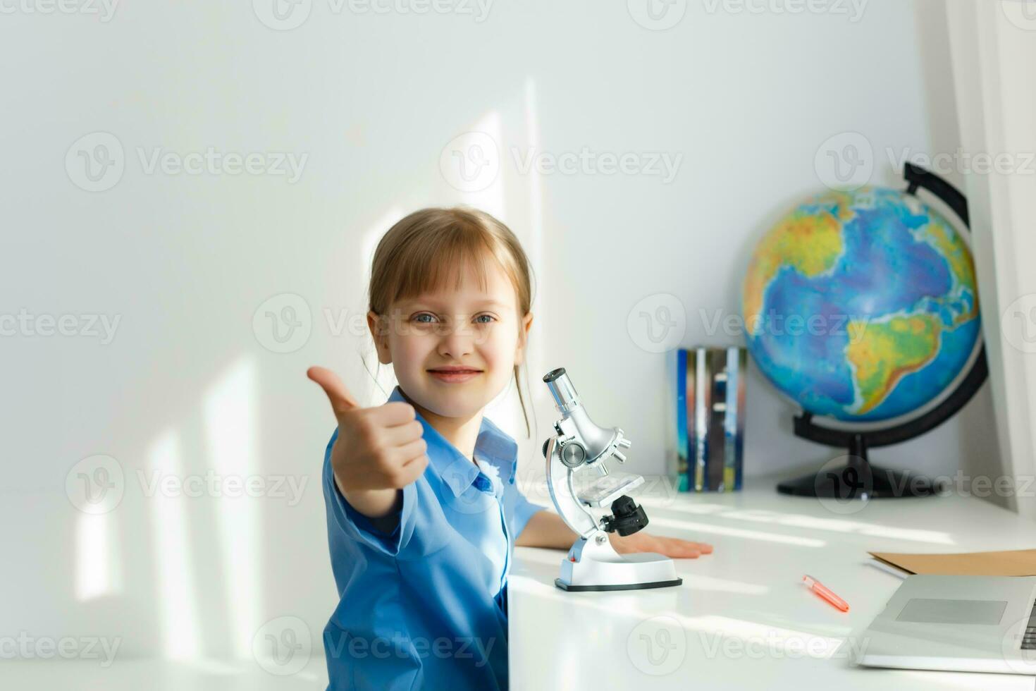 Cute little girl is sitting at table with her laptop and studying online photo