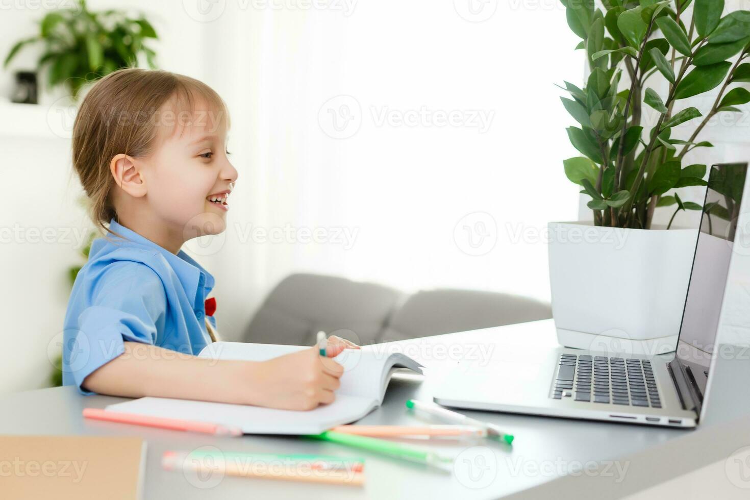 Cute little girl is sitting at table with her laptop and studying online photo