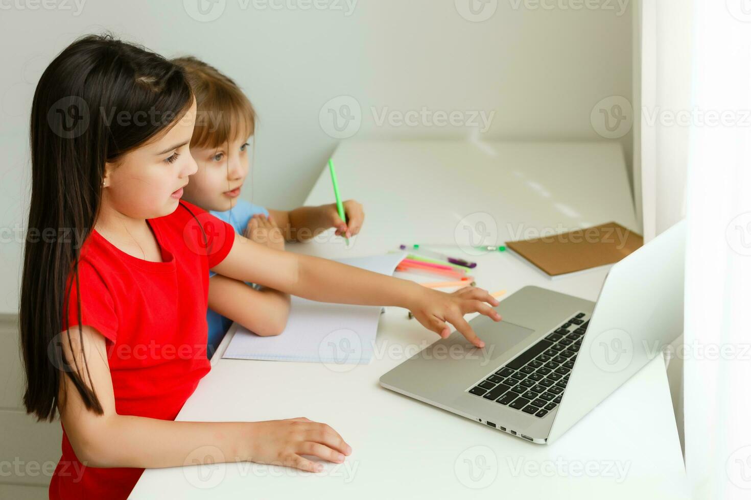 Two girls, the oldest and the youngest, are engaged at a table on a laptop. photo