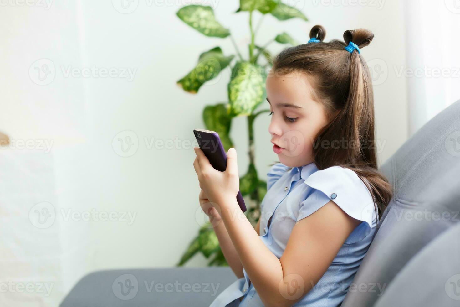 Distance learning, online education for kids. Little girl studying at home in front of the smartphone. Child watching online cartoons, kids computer addiction, parental control. Quarantine at home photo