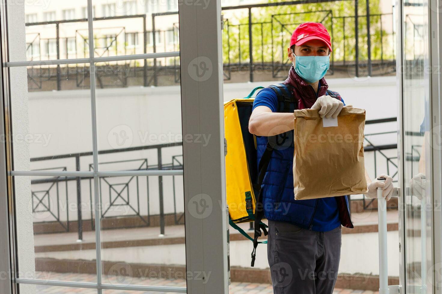 Delivery Man standing with yellow thermo backpack for food delivery near the entrance home with empty space to copy paste photo