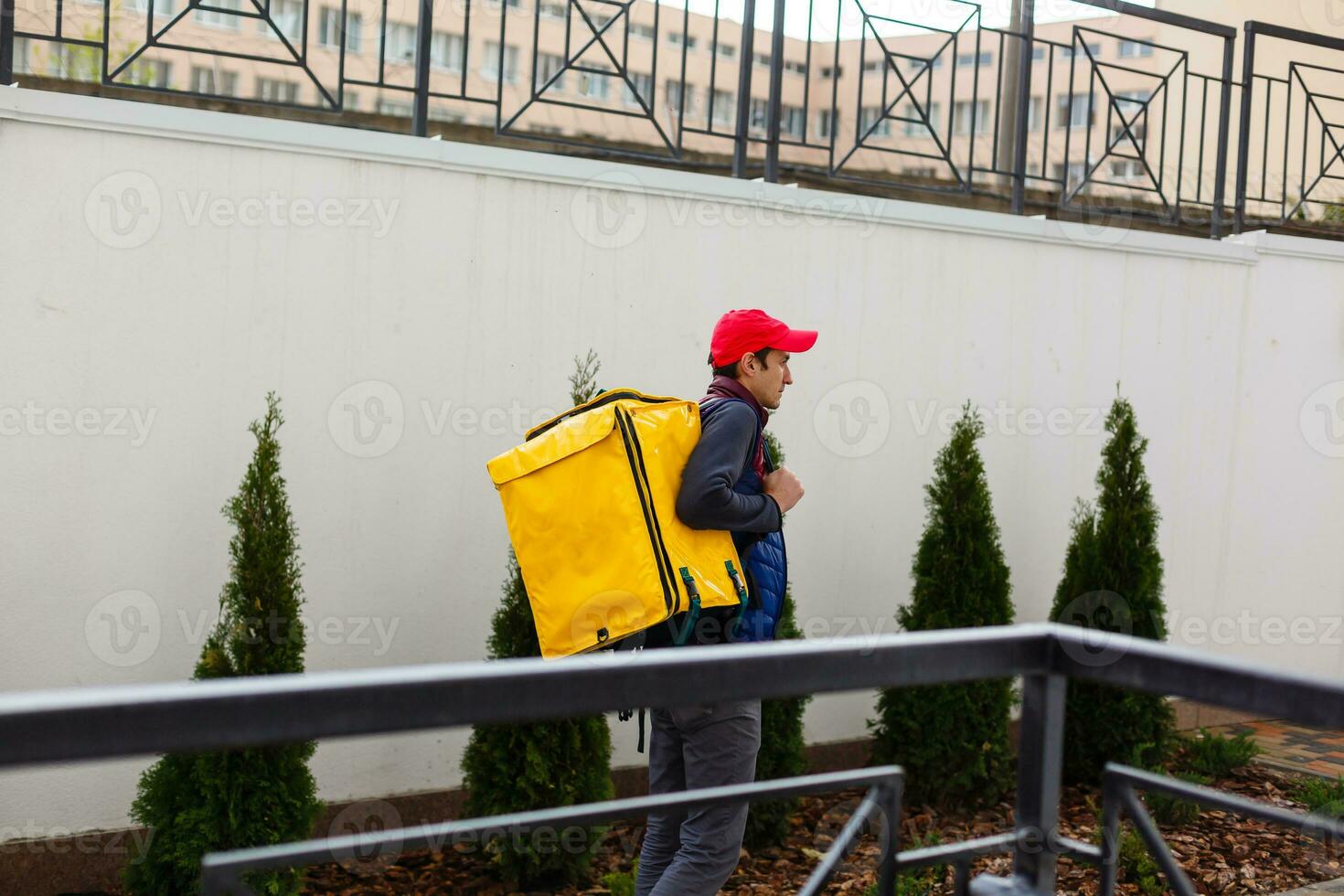 Delivery Man standing with yellow thermo backpack for food delivery near the entrance home with empty space to copy paste photo