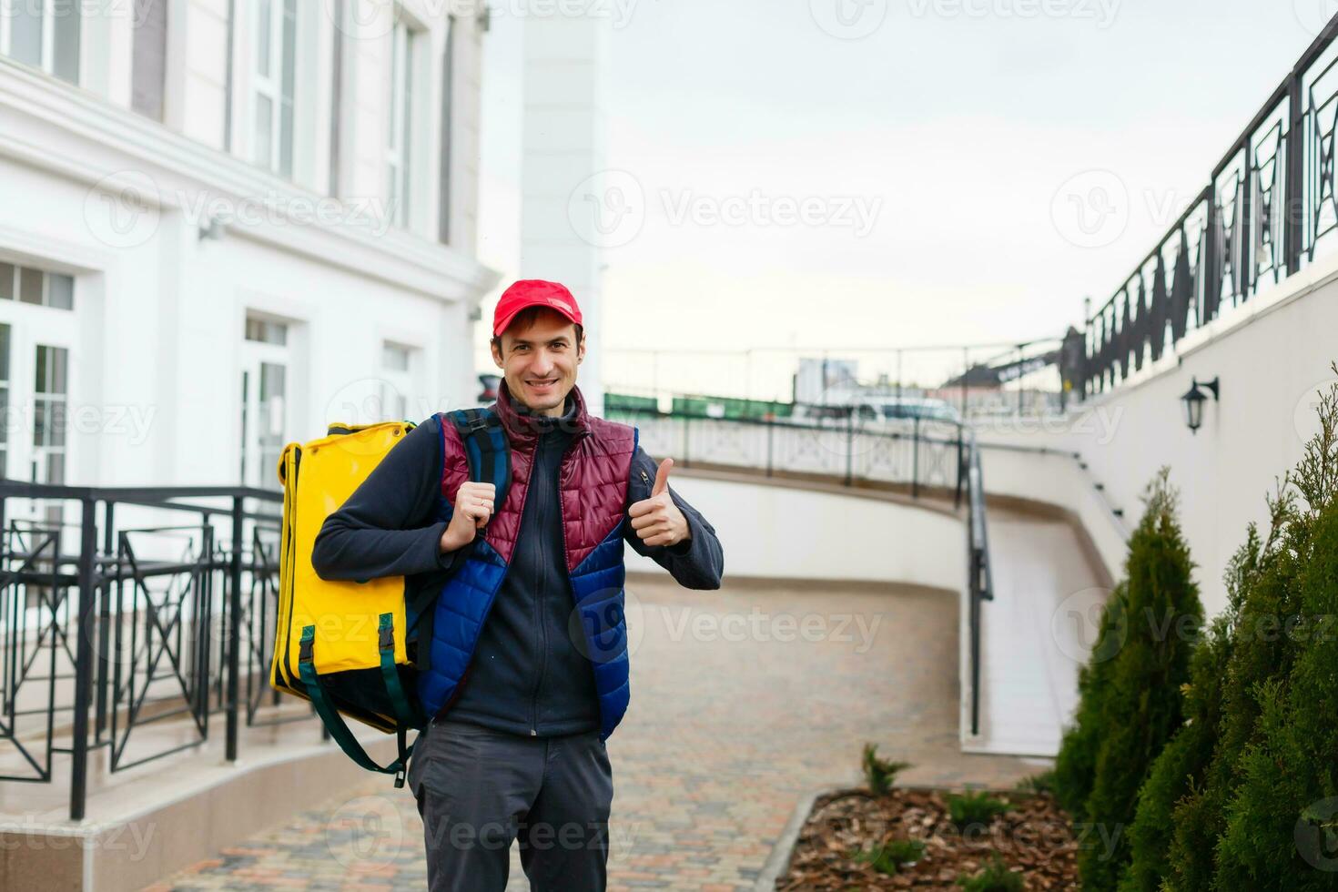 Portrait of a cheerful delivery man standing with yellow thermo backpack for food delivery on the street outdoors photo