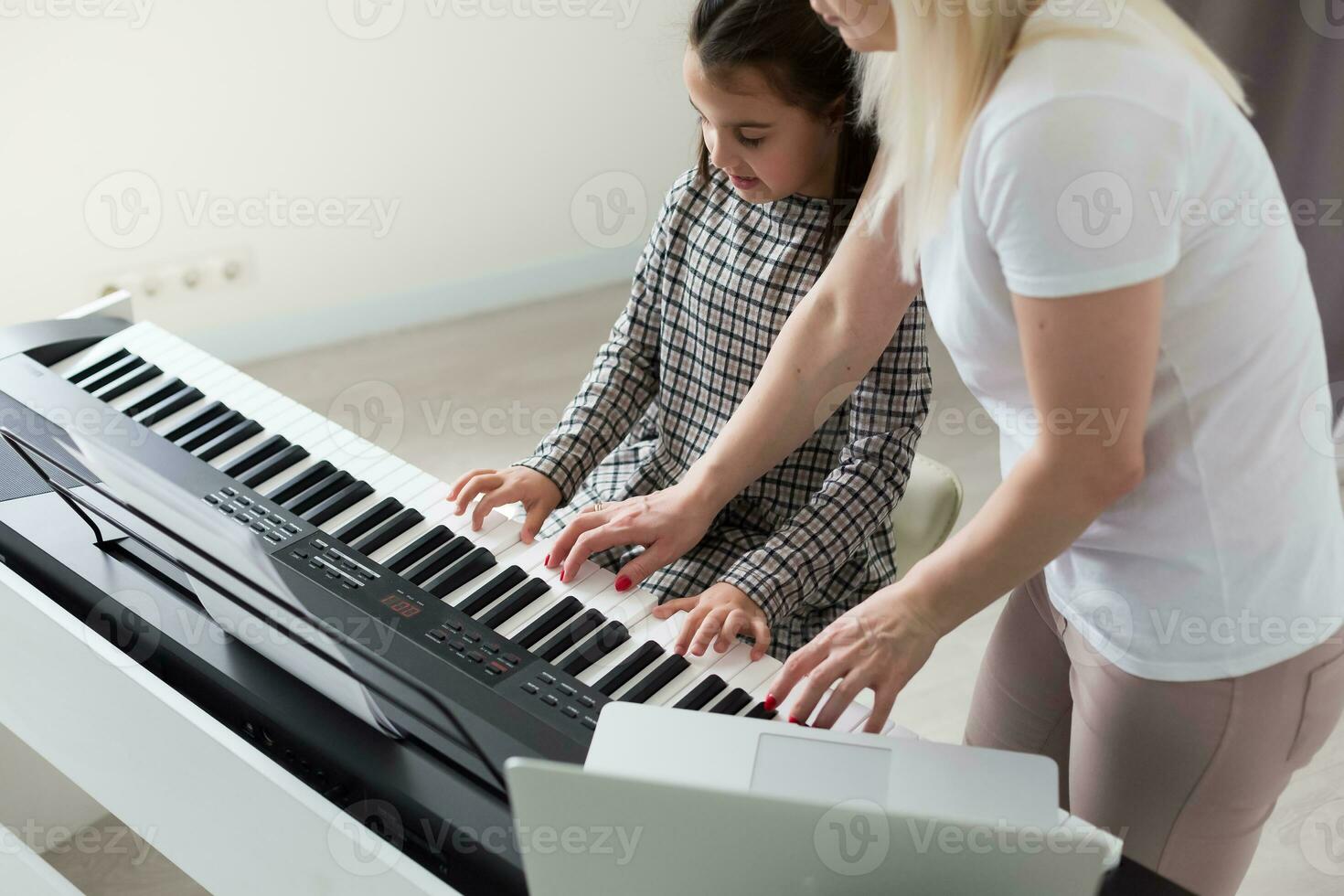 Woman helping her daughter to play the piano, body and buttons of the piano were digitally modified photo