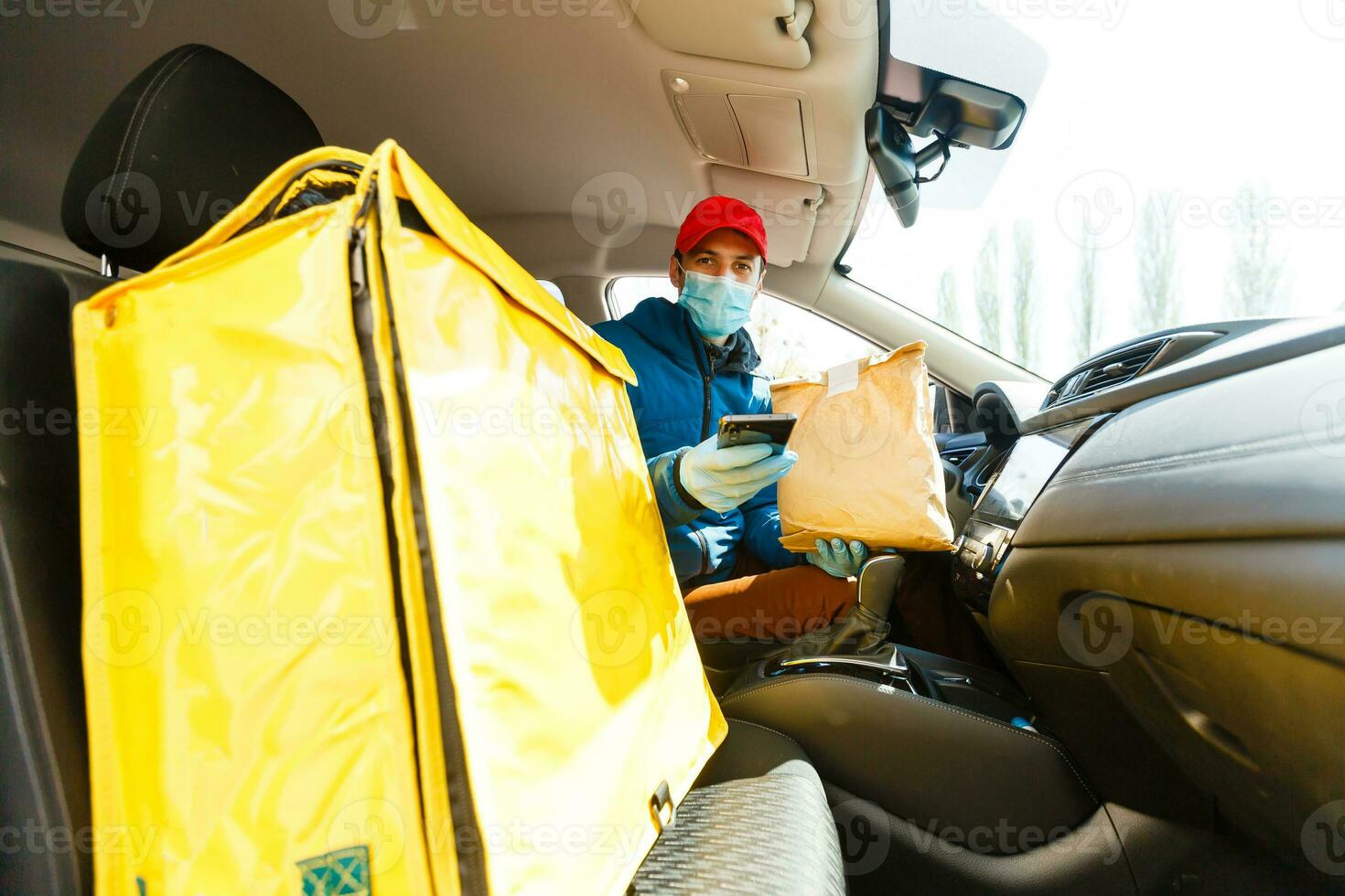 food delivery man in a protective mask and gloves with a thermo backpack near a car during the quarantine period photo