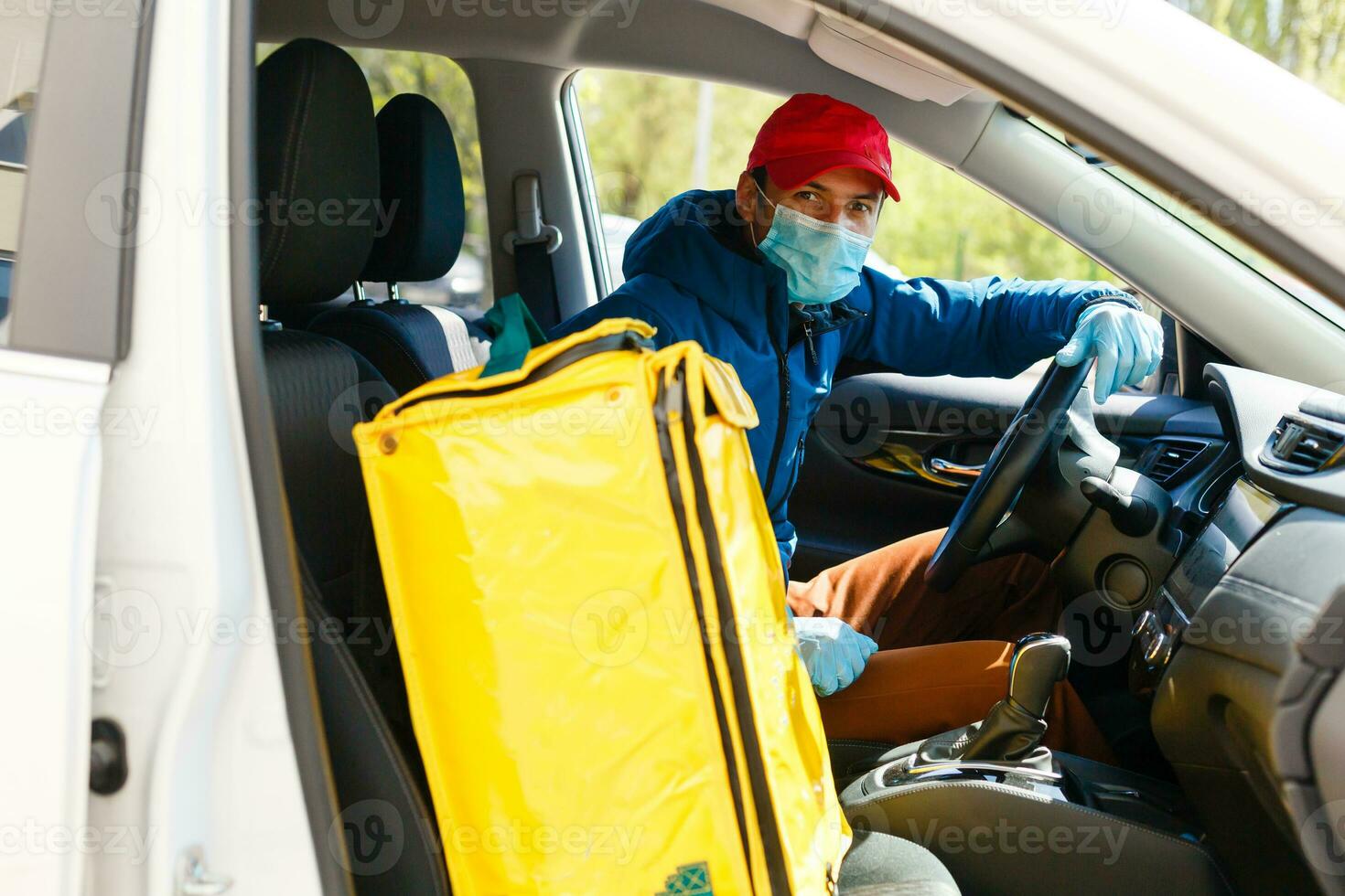 food delivery man in a protective mask and gloves with a thermo backpack near a car during the quarantine period photo