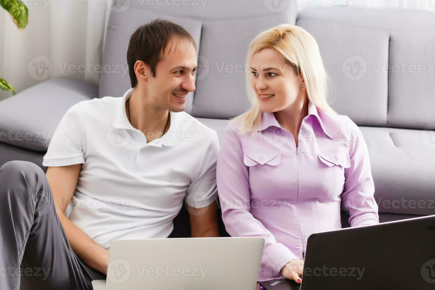 Happy young casual couple sitting working together at home office, smiling. photo