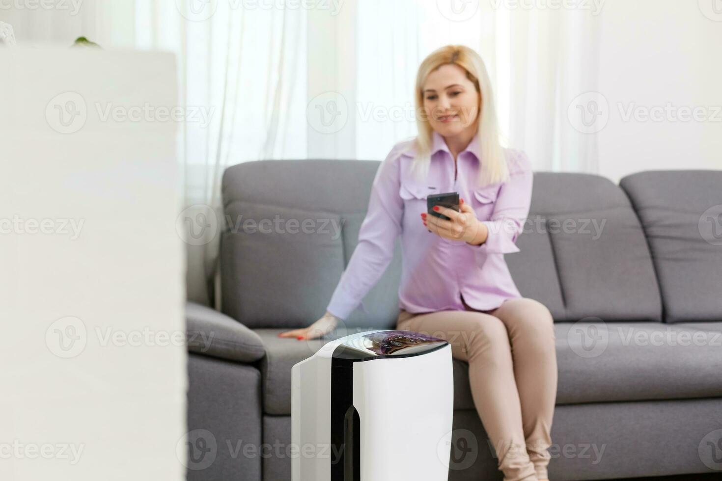 joven mujer relajante en el sofá mientras aire humidificador o purificador trabajando en el primer plano. controlador eso con un teléfono inteligente remotamente foto