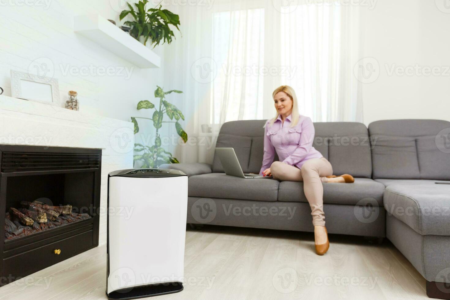 aire purificador en un vivo habitación, mujer trabajando con ordenador portátil con filtrar para limpiar habitación foto