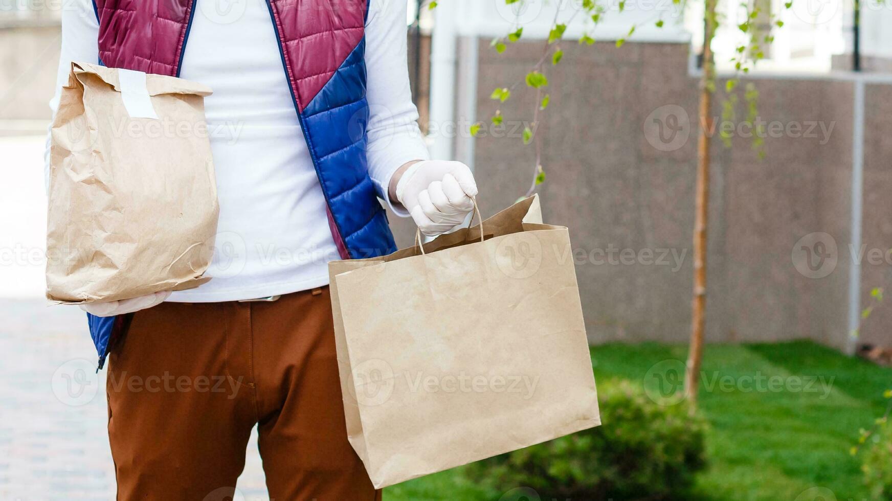 Courier in protective mask and medical gloves delivers takeaway food. Delivery service under quarantine, disease outbreak, coronavirus covid-19 pandemic conditions. photo