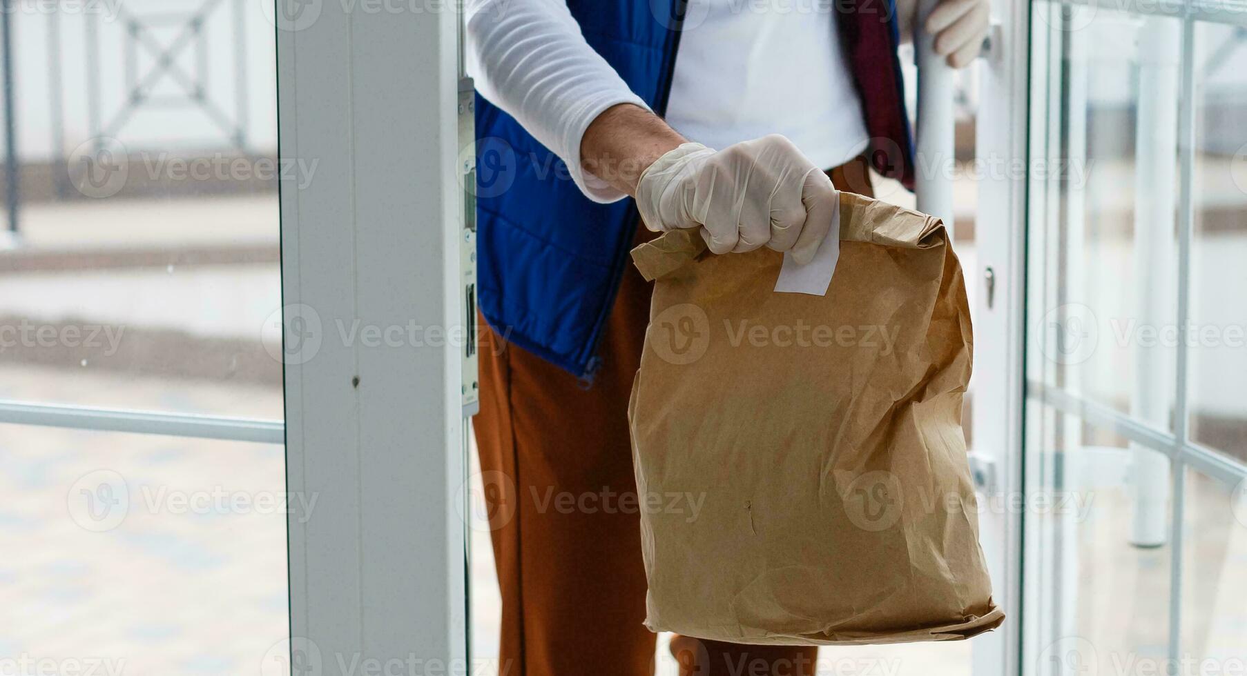 Delivery man holding paper bag with food on white entrance of house background , food delivery man in protective mask photo