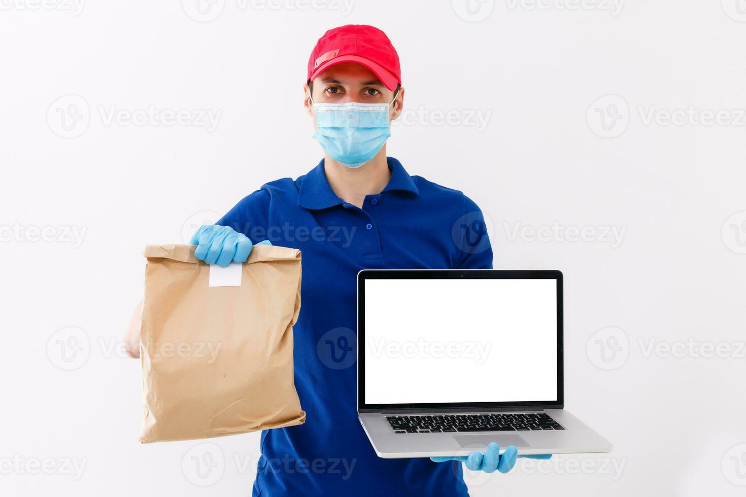 Delivery man in red cap blank t-shirt uniform mask gloves isolated on white background, Guy employee work hold laptop computer, Service quarantine pandemic coronavirus virus 2019-ncov concept photo