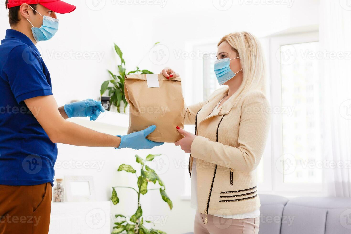Man from delivery service in red cap, in protective mask and gloves giving food order and holding boxes over white background photo