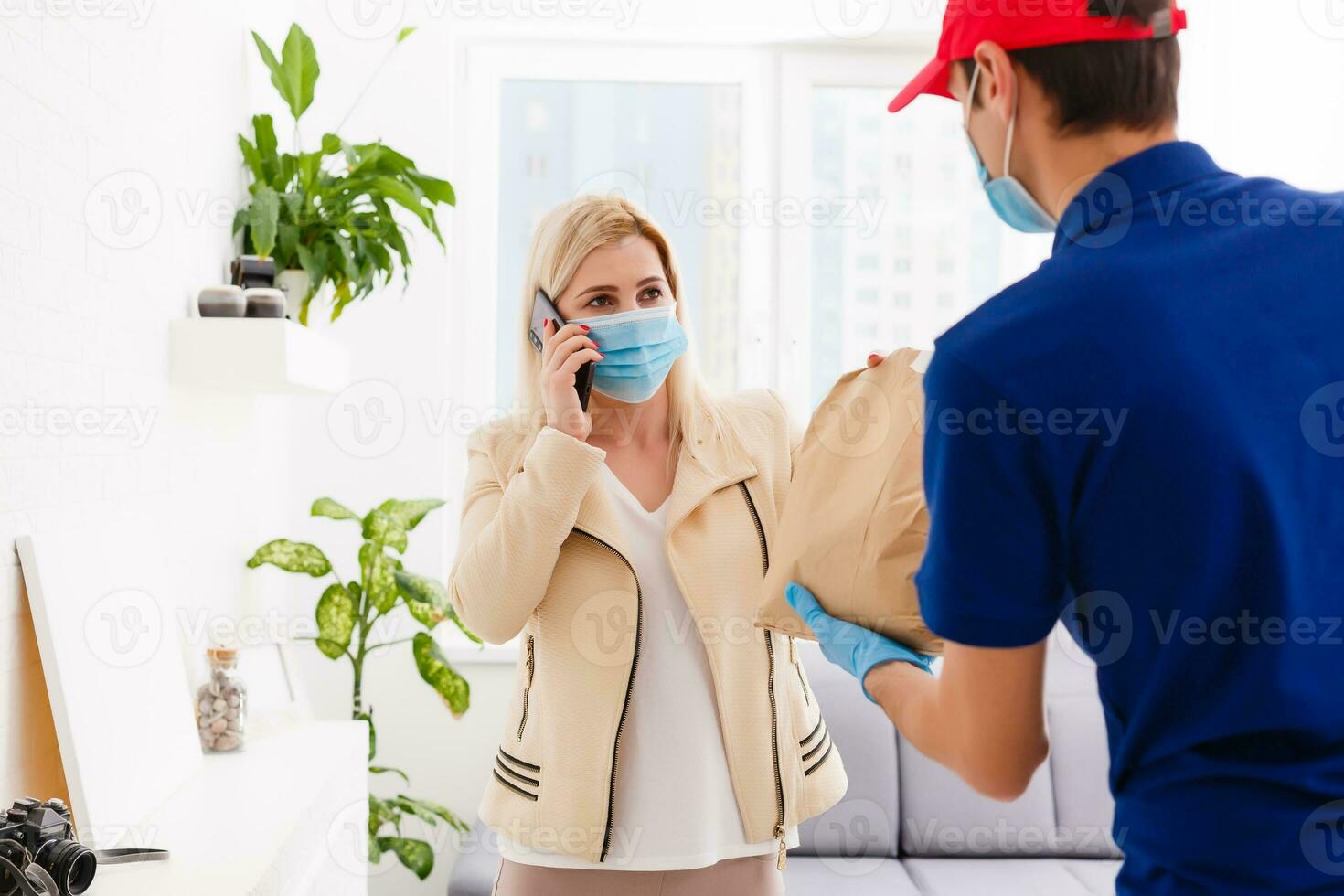 Man from delivery service in red cap, in protective mask and gloves giving food order and holding boxes over white background photo