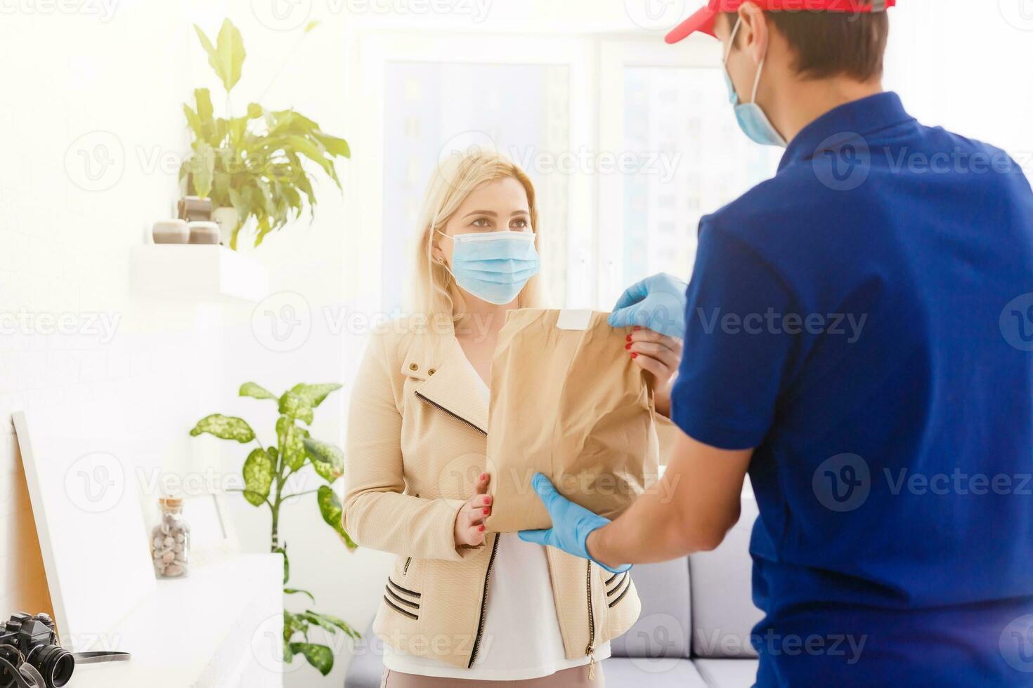 Man from delivery service in red cap, in protective mask and gloves giving food order and holding boxes over white background photo