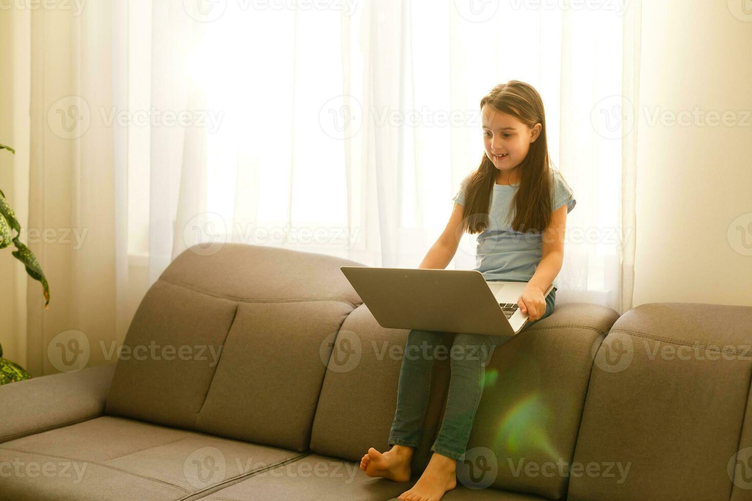 Remote lessons. The child smiles happily and gets knowledge remotely. Little girl study online learning from home with laptop. Online school. photo