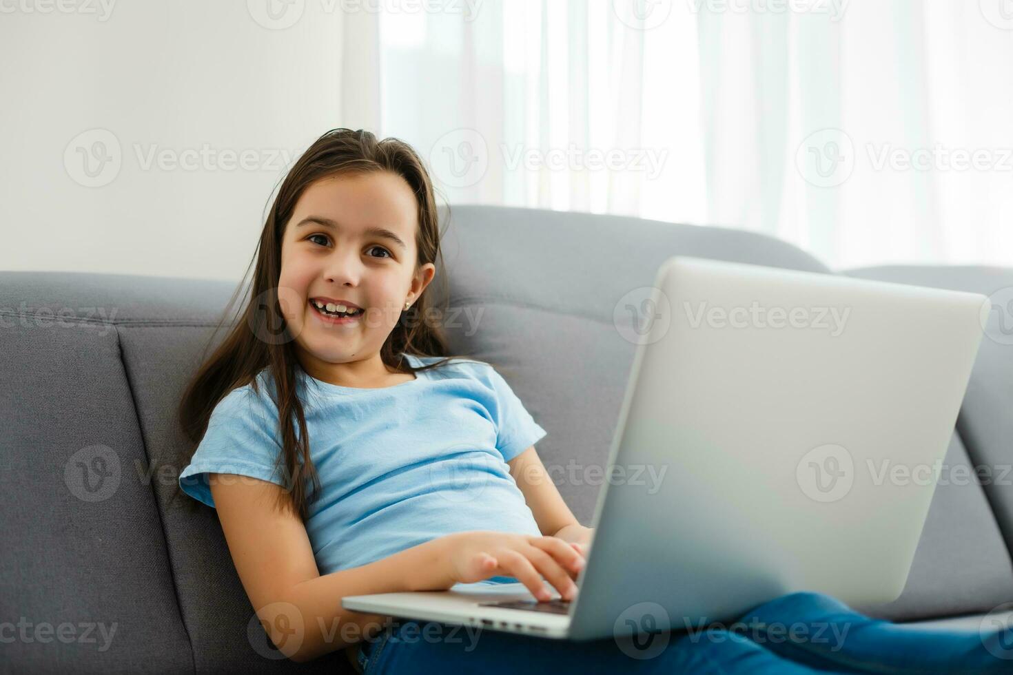 Head shot close up portrait of happy small pupil learning at home. Smiling little child girl enjoying doing lessons in living room. Smart kid schoolgirl looking at camera, studying remotely online. photo