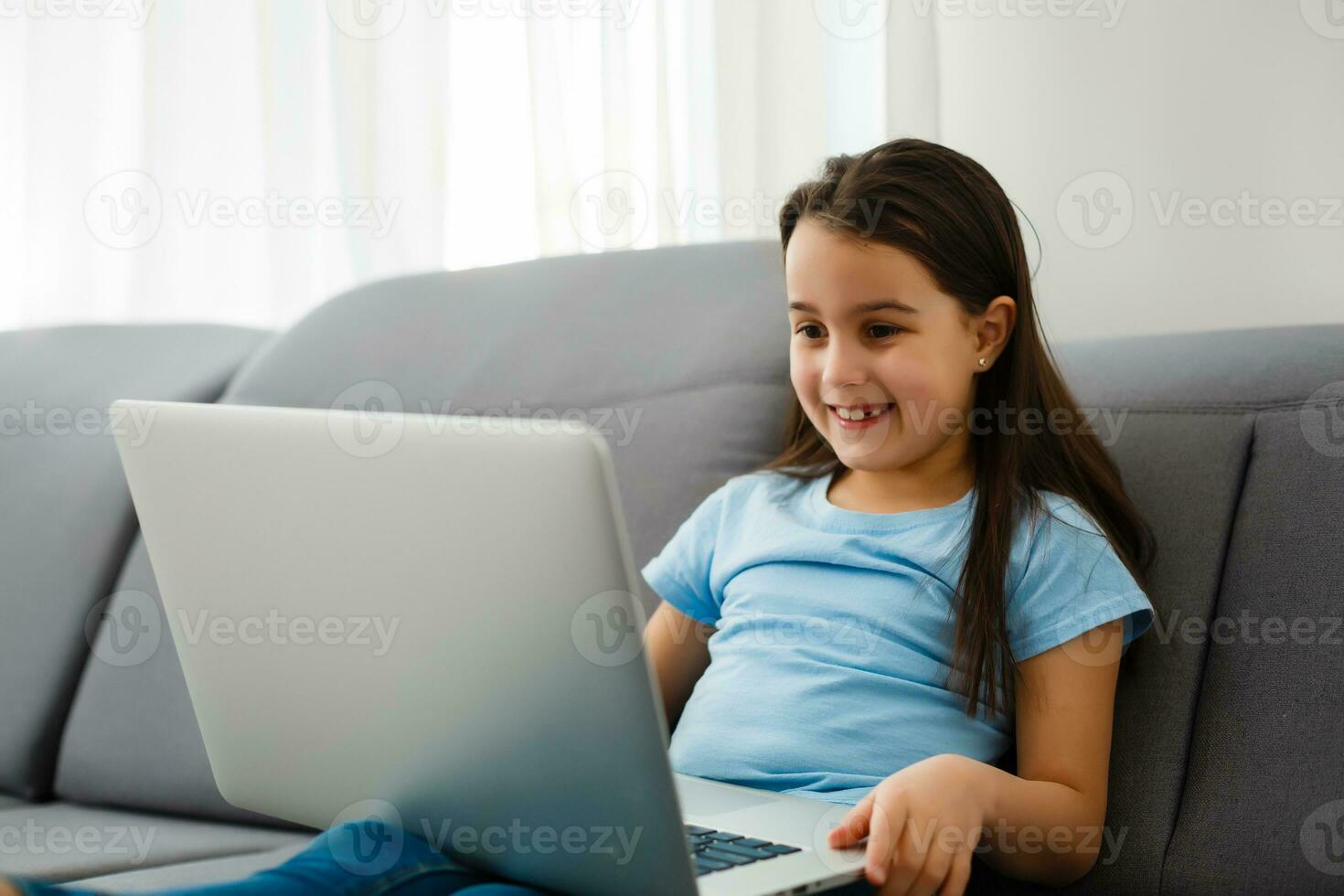 Head shot close up portrait of happy small pupil learning at home. Smiling little child girl enjoying doing lessons in living room. Smart kid schoolgirl looking at camera, studying remotely online. photo