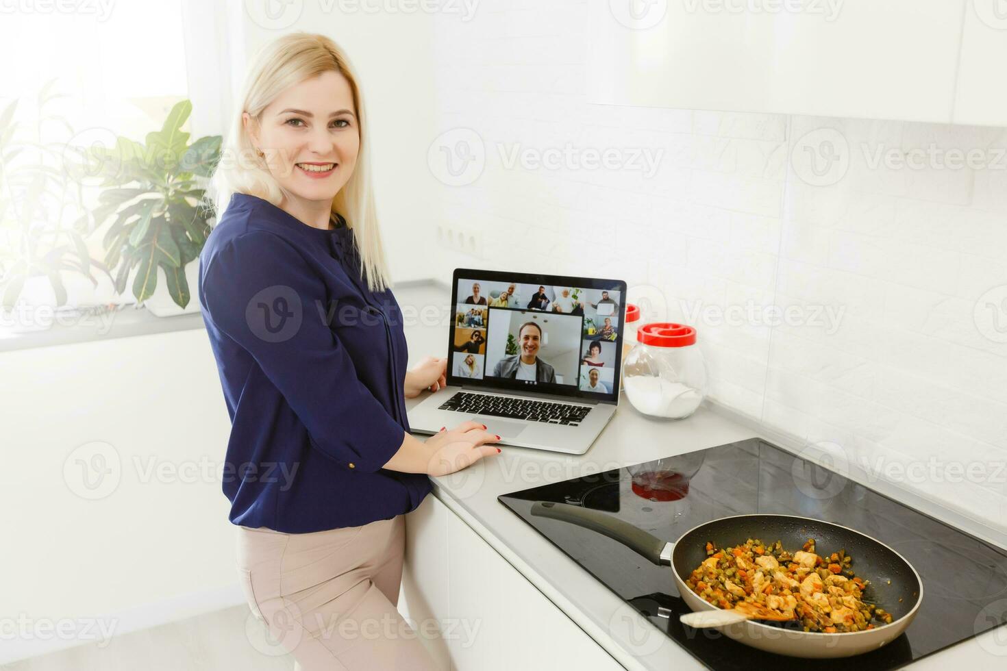 Beautiful girl is learning to cook healthy food online by the internet from a laptop in gray kitchen on table. photo