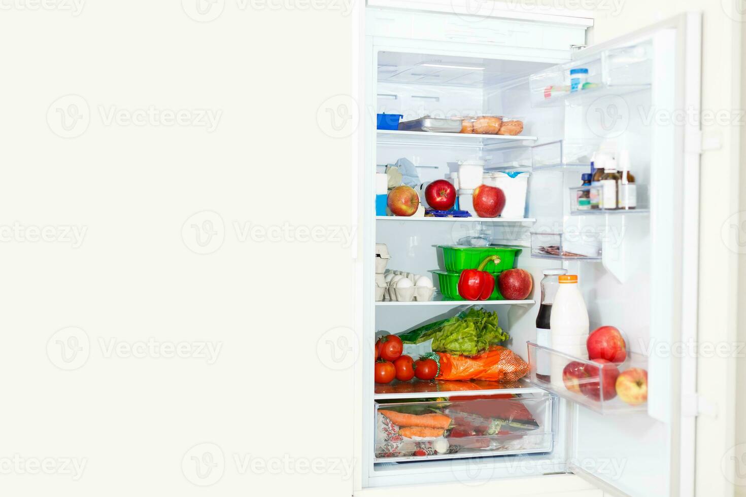 Top freezer kitchen refrigerator with doors open and shelves full of groceries with fresh and frozen food and cold bottles photo