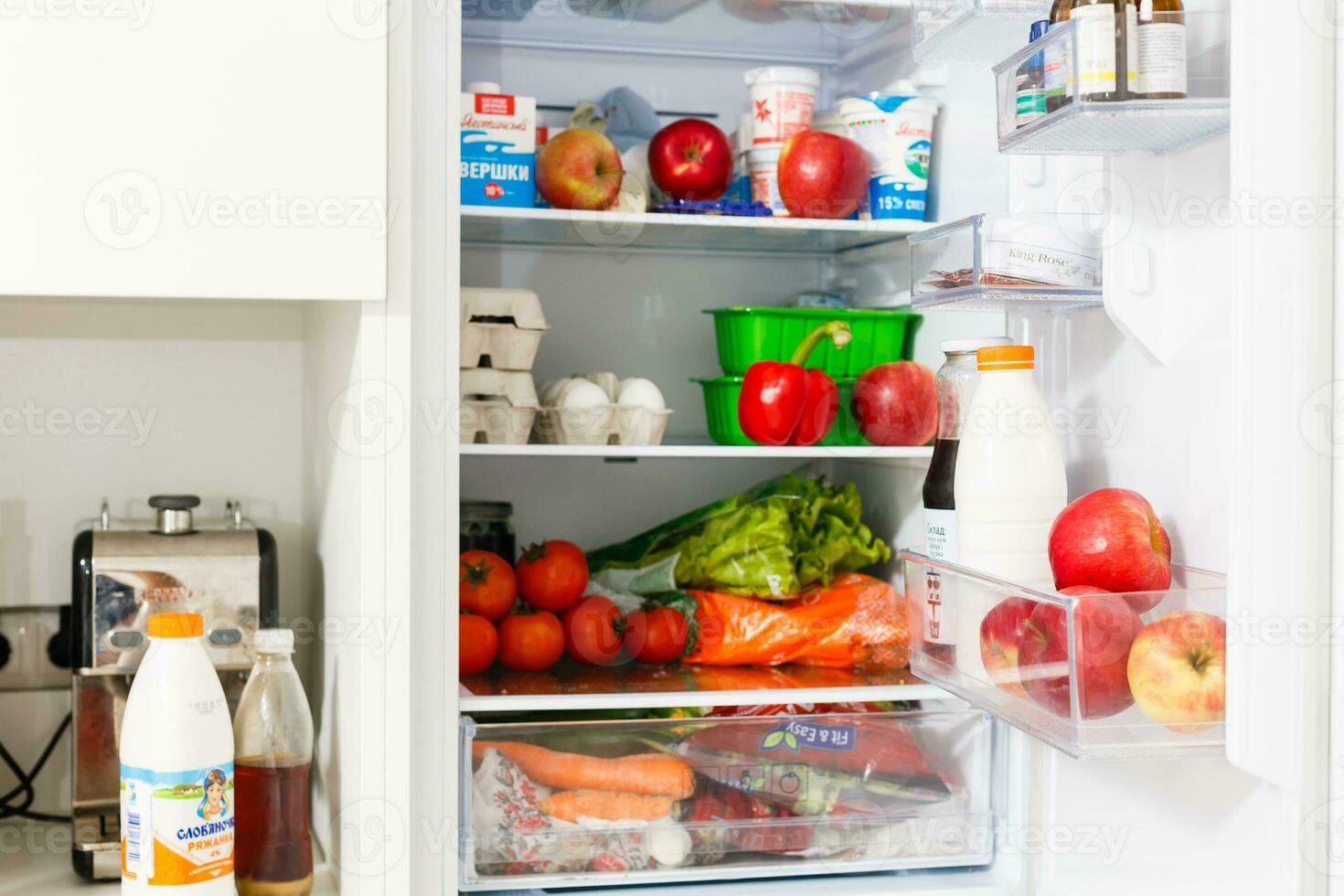 Top freezer kitchen refrigerator with doors open and shelves full of groceries with fresh and frozen food and cold bottles photo