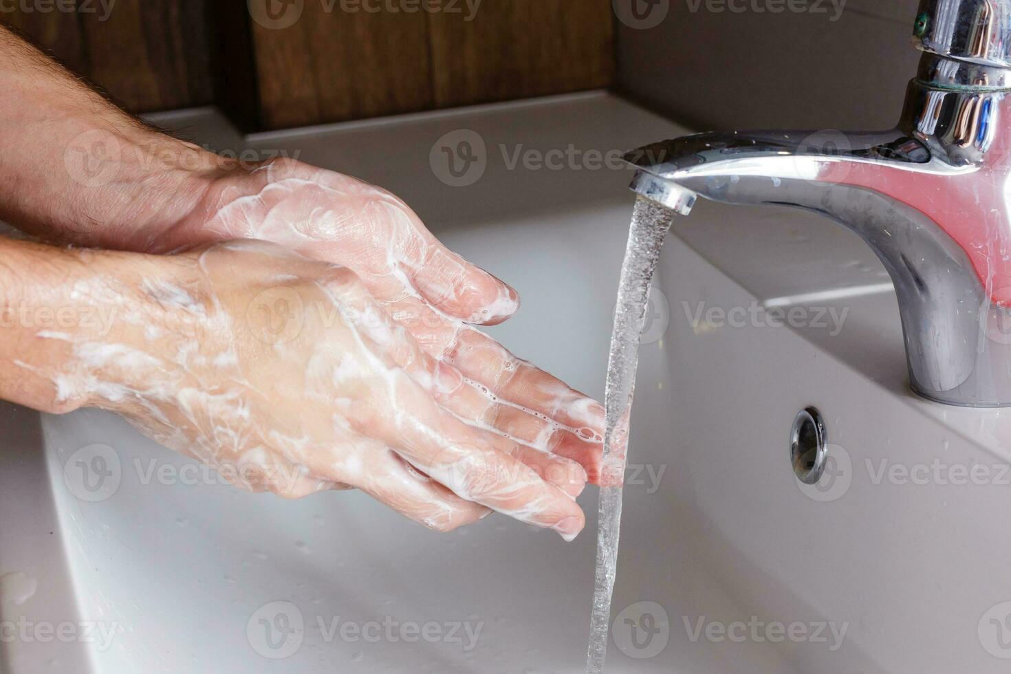 man washes his hands near the white washbasin photo