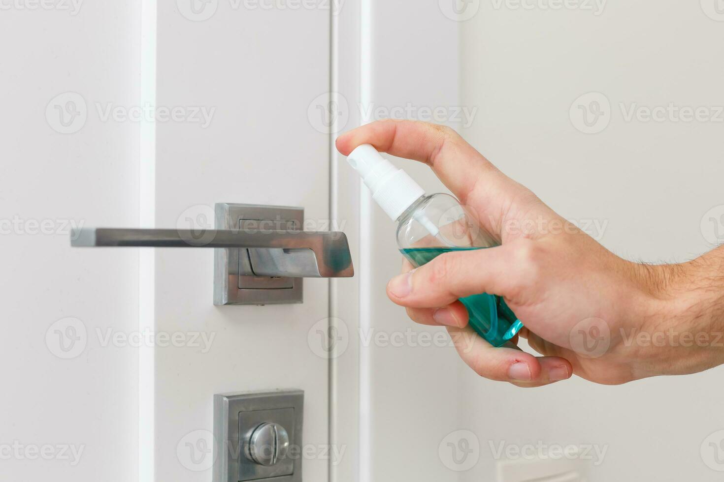 Hands hold the sprayer with an antiseptic, the other - wipes the door handle with a cloth moistened with a disinfectant solution photo