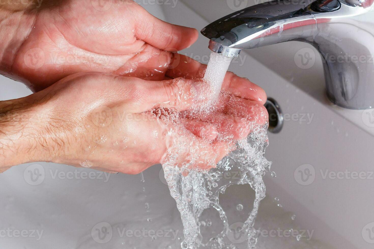 man washes his hands near the white washbasin photo