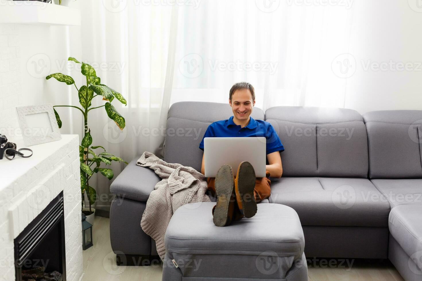 Happy young man in t-shirt sitting at home, working on laptop computer, smiling. photo