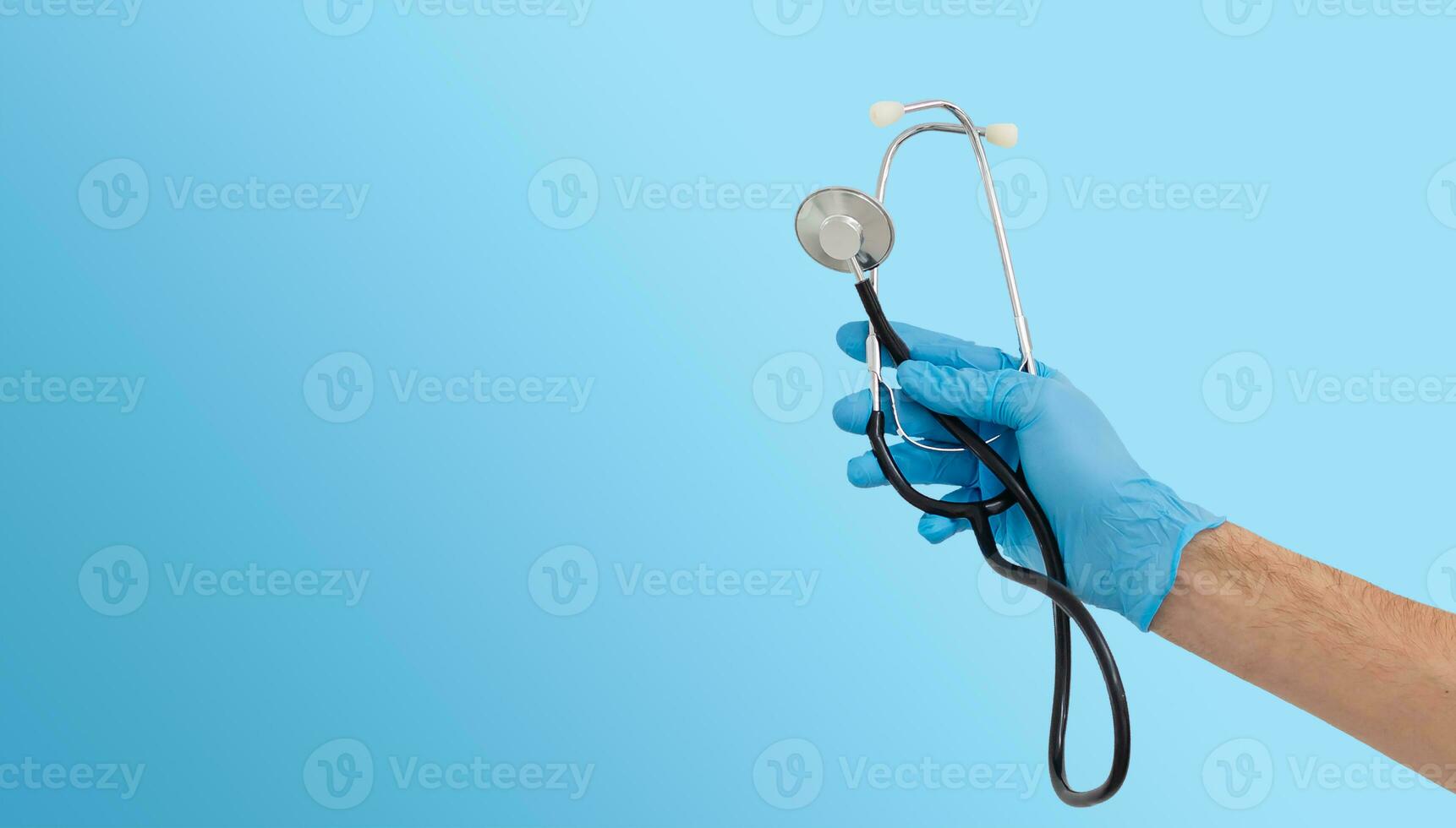 Caucasian male hand, wearing medical gloves, holding a stethoscope, white background photo